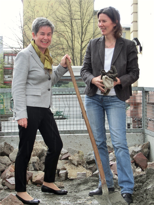 Zwei Frauen stehen beieinander, eine mit Schaufel in der Hand.