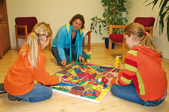 Frau mit zwei Mädchen am Boden sitzend bei Malaktion