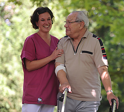 Alter Mann mit Rollator und Altenpflegerin im Freien