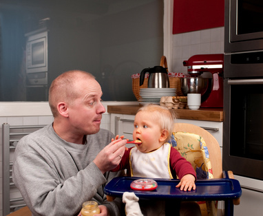 Ein junger Vater gibt seinem Kind Brei.