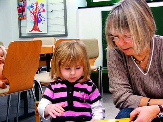 Familienpatin schaut mit kleinem Mädchen ein Buch an.