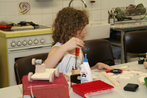 Zu sehen ist ein junges Mädchen, welches einen Schraubenzieher in der Hand hält. Sie blickt nach rechts, dies erweckt den Anschein, dass sie jemandem zuhört.