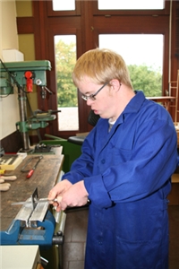 Werkstatt_02 Wir sehen einen Werkstattarbeiter der Metall durchsägt. Er trägt einen Blauen Arbeiteranzug.