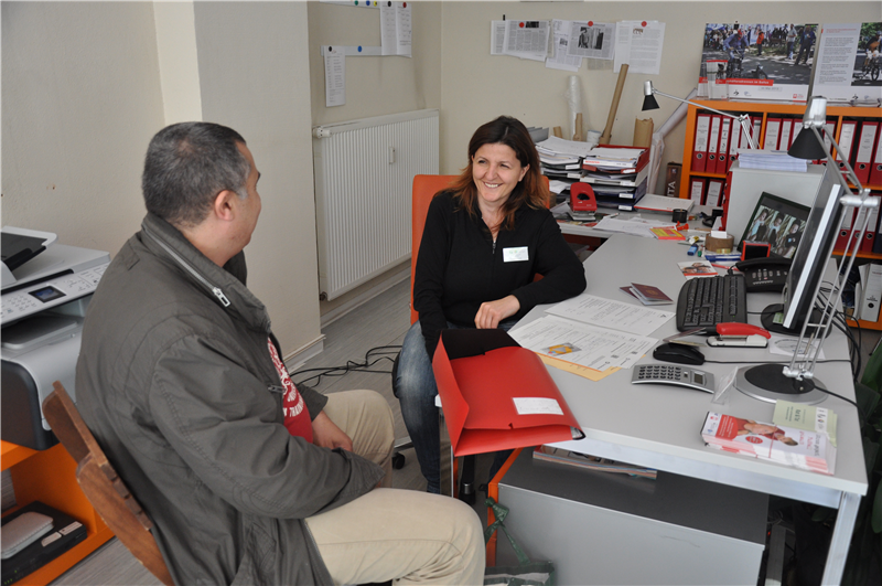 Auf dem Bild ist die ehrenamtliche Beraterin Shpresa Ajvazi im Quartiersbüro mit einem ratsuchenden Nachbarn zu sehen