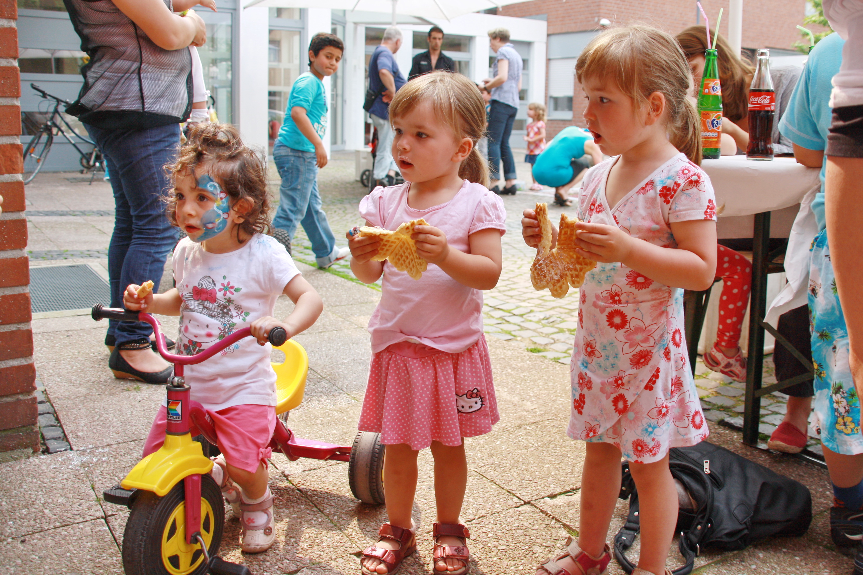 Auf dem Foto stehen drei rosa gekleidete Kleinkinder