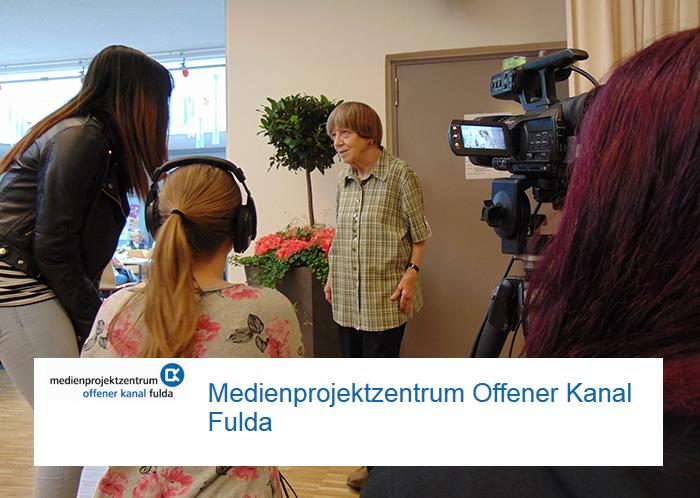 Wir schauen zu, wie Altenpflegeschüler mit einer professionellen Kamera eine Seniorin bei Heraustreten aus ihrem Zimmer filmen. 