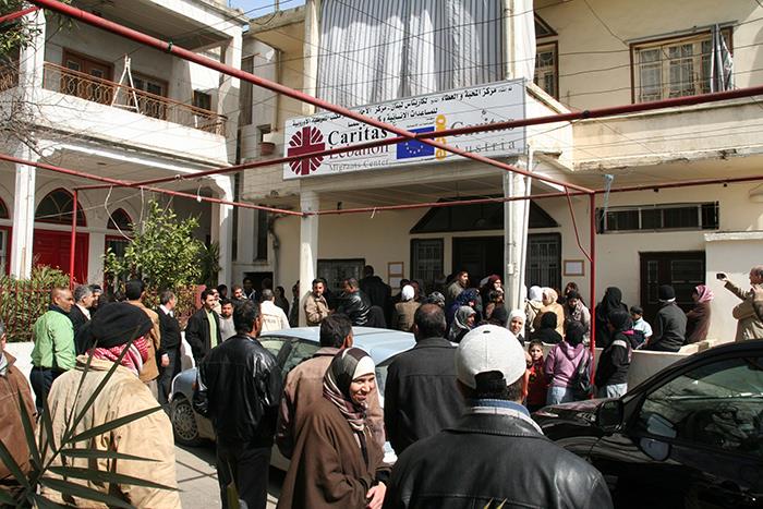 Wir befinden uns auf einem Platz in Bekaa vor einem Caritas-Haus. Über der Tür ist ein großes Plakat der Caritas angebracht. Viele Menschen suchen dort Zuflucht!