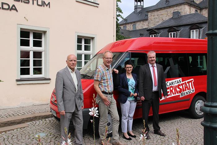 Vor der Geschäftsstelle des Caritasverbandes steht ein roter Fort-Bus mit der Aufschrift Caritas Werkstatt Mensch. Vor ihm stehen 4 Personen, die in die Ukraine fahren werden.