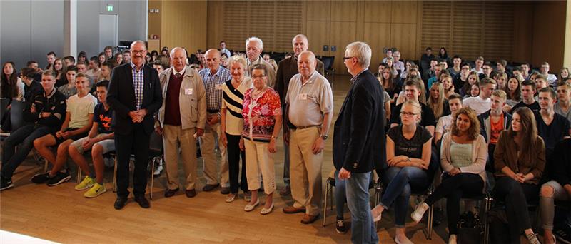 In der Aula des Marianums haben sich die Zeitzeugen mit den Verantwortlichen in den Mittelgang zu den voll besetzten Schülerreihen gestellt. Gemeinsam mit den Schülern blicken sie uns an. 
