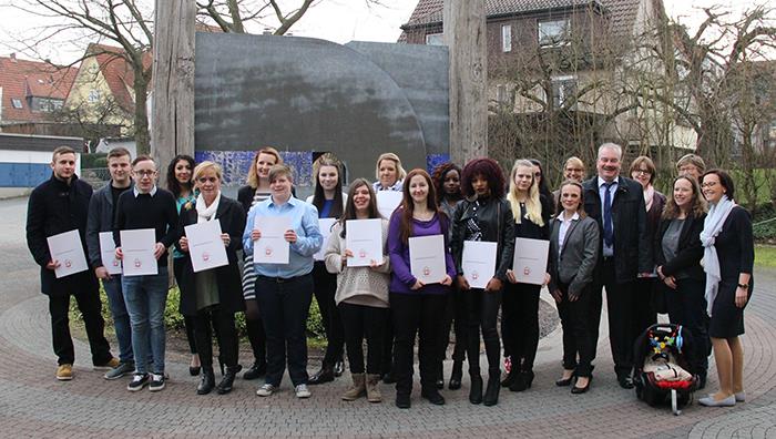 Die Gruppe der Absolventen haben sich mit ihren Lehrern und den Verantwortlichen der Caritas zu einem Gruppenfoto vor einem Kunstwerk auf dem Gelände der Behindertenhilfe zusammen gestellt.