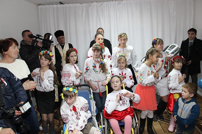 Viele Kinder und Jugendliche haben sich in ihrer Trachten zu einem Gruppenfoto zusammengestellt. Ihre Eltern und Angehörigen haben sich am Rand zusammen gestellt. Zwei Kinder in der vorderen Reihe sitzen im Rollstuhl. Viele Mädchen tragen einen Blumenkranz in ihren Haaren. 