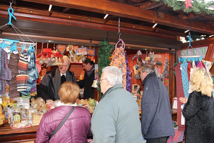 Wir schauen 4 Käufern über den Rücken in den bunt geschmückten und hell erleuchteten Weihnachtsstand der Caritas-Werkstätten. In ihm ist unser Generalvikar Prof. Dr. Stanke als Verkäufer. Er unterhält