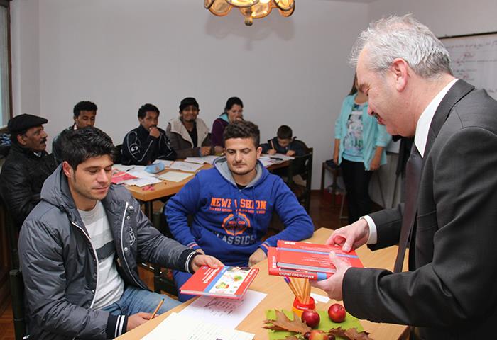 Unser Caritasdirektor ist Gast im Sprachkurs der Volkshochschule. Er ist im Unterrichtsraum und verteilt  Bücher.