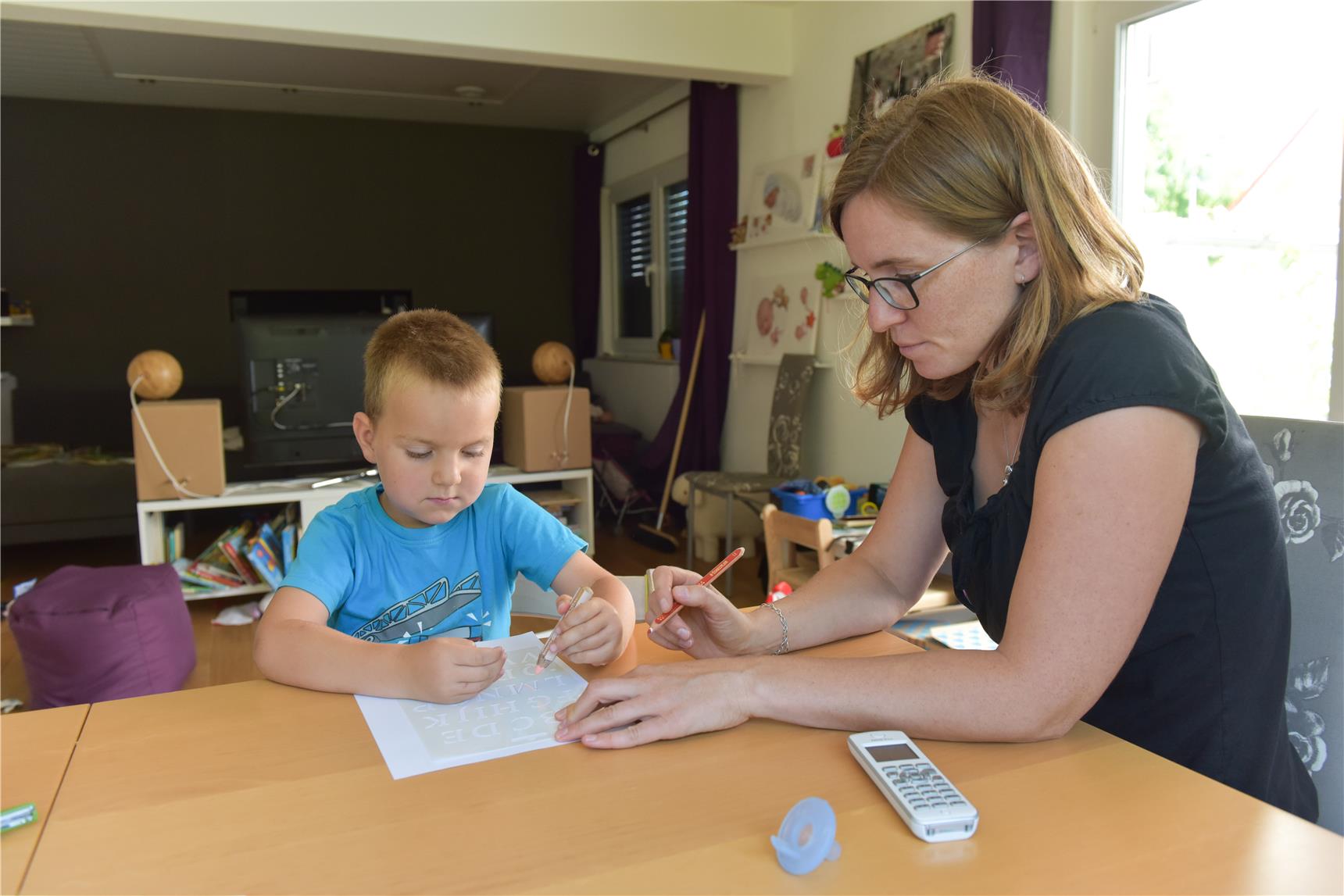 Frau sitzt mit Kind am Tisch und bearbeitet eine Schulaufgabe