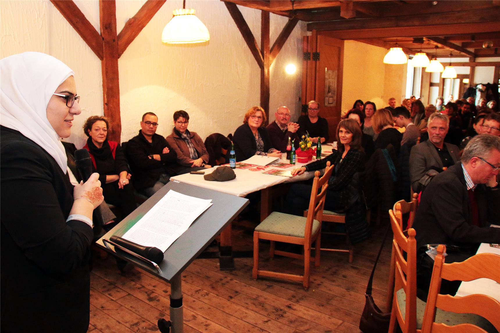 Eine Frau steht am Rednerpult und erzählt vielen Menschen etwas.