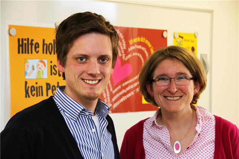 Das Foto zeigt einen Mann und eine Frau vor einem farbenfrohen Hintergrund stehend.