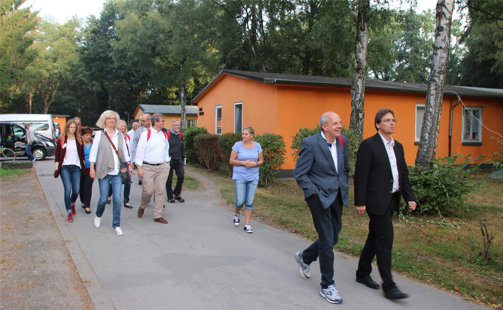 Das Foto zeigt eine Gruppe von Menschen, die auf einer Straße ein niedriges Gebäude passiert.