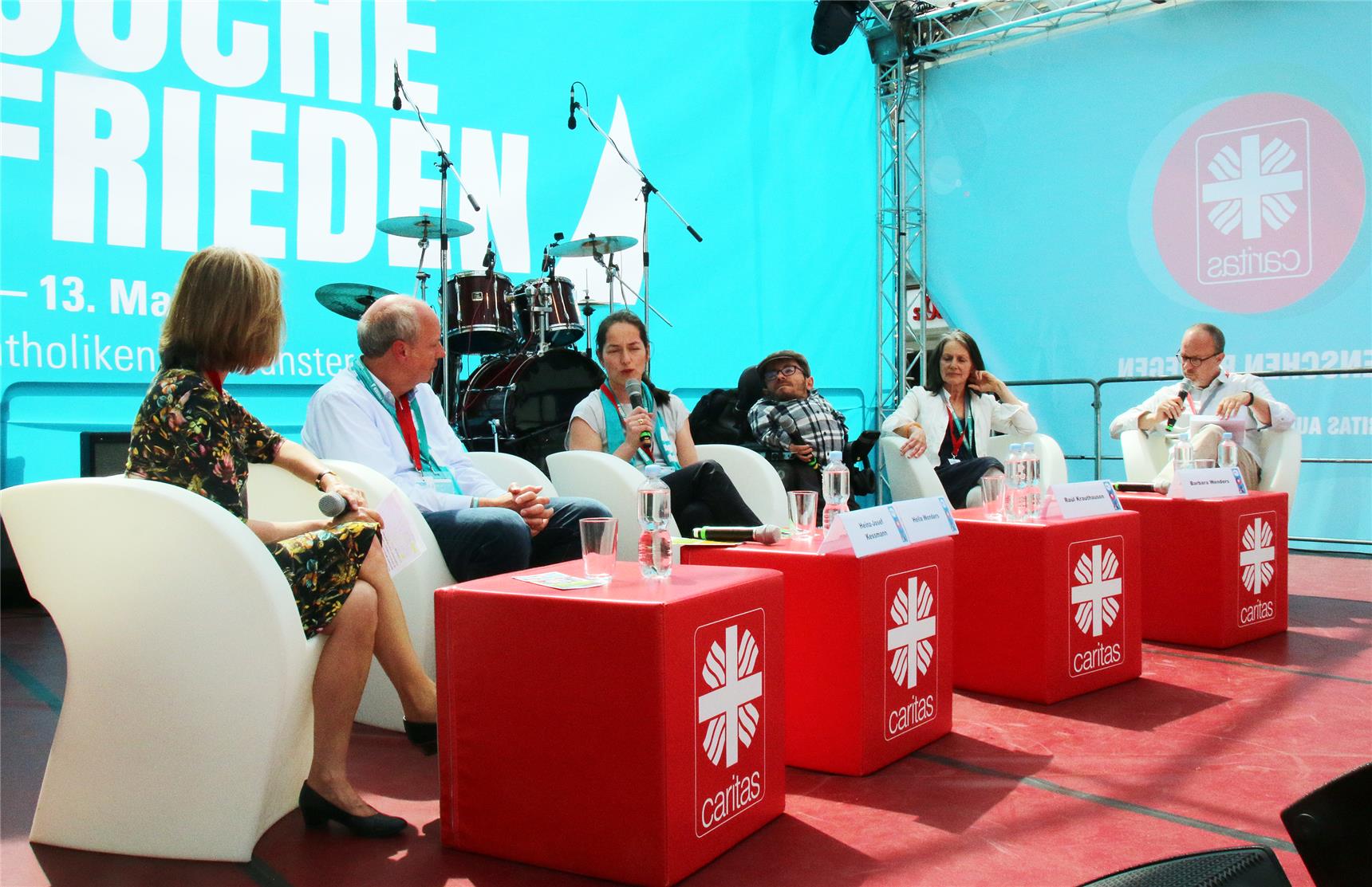 Das Foto zeigt eine Gruppe Menschen, die in weißen Stühlen in einer Reihe auf einer Bühne sitzen.