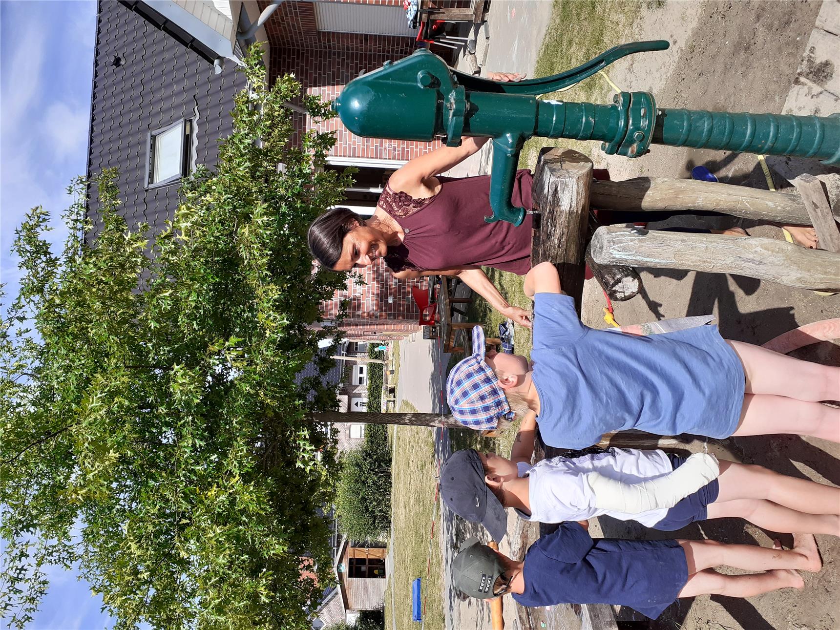 Das Foto zeigt eine Frau und vor ihr an einer Wasserpumpe stehend drei Kinder.