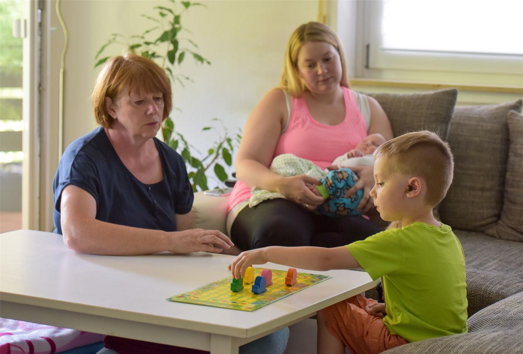 Das Foto zeigt zwei Frauen an einem Wohnzimmertisch, die mit einem Jungen ein Brettspiel spielen.