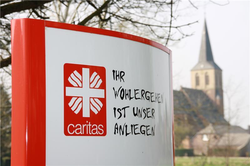 Das Foto zeigt eine Stele mit dem Logo des Caritasverbandes Geldern-Kevelaer und im Hintergrund leicht verschwommen einen Kirchturm.