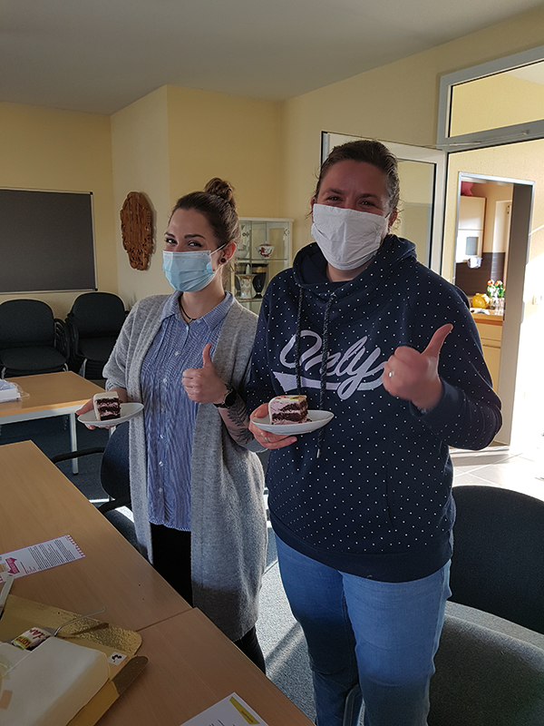 Nadine Heimüller und Nicole Rethmeier von der Fachberatungsstelle für Wohnungslose des SKM in Paderborn, die einen Teller mit einem Tortenstück hochhalten und einen Daumen nach oben zeigen