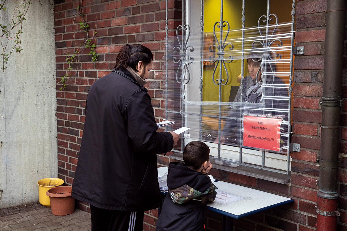 Ein Bewohner des Wilhelm-Sternemann-Hauses mit Kind, der mit einer Mitarbeiterin durch ein mit Folie gesichertes Fenster redet