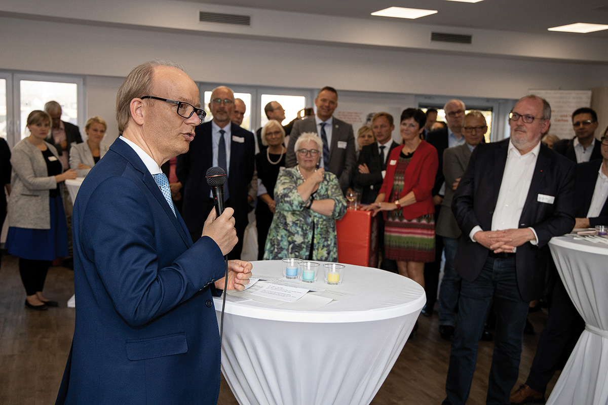 Landtagspräsident André Kuper steht an einem Stehtisch mit einem Mikrofon in der Hand und hält auf dem Parlamentarischen Abend der CiNW sein Grußwort. Im Hintergrund sind die Gäste des Abends zu sehen