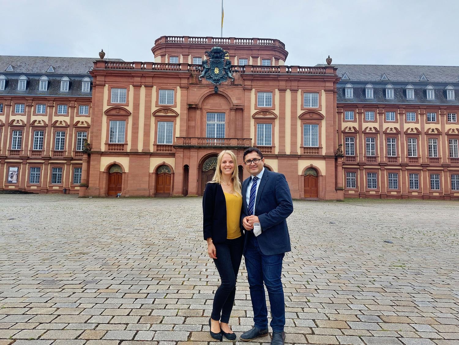 Eine junge blonde Frau und ein junger mann mit dunklem kurzem haar und Brill stehen vor der Universität Mannheim.