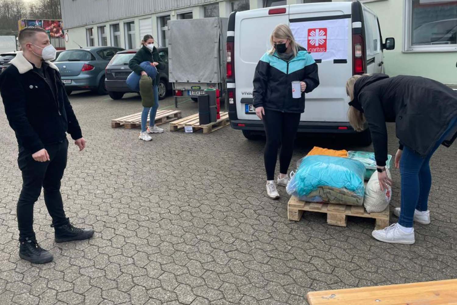 Zwei Fra8uen und ein Mann stehen vor einem weißen Lieferwagen mit Caritas-Logo.