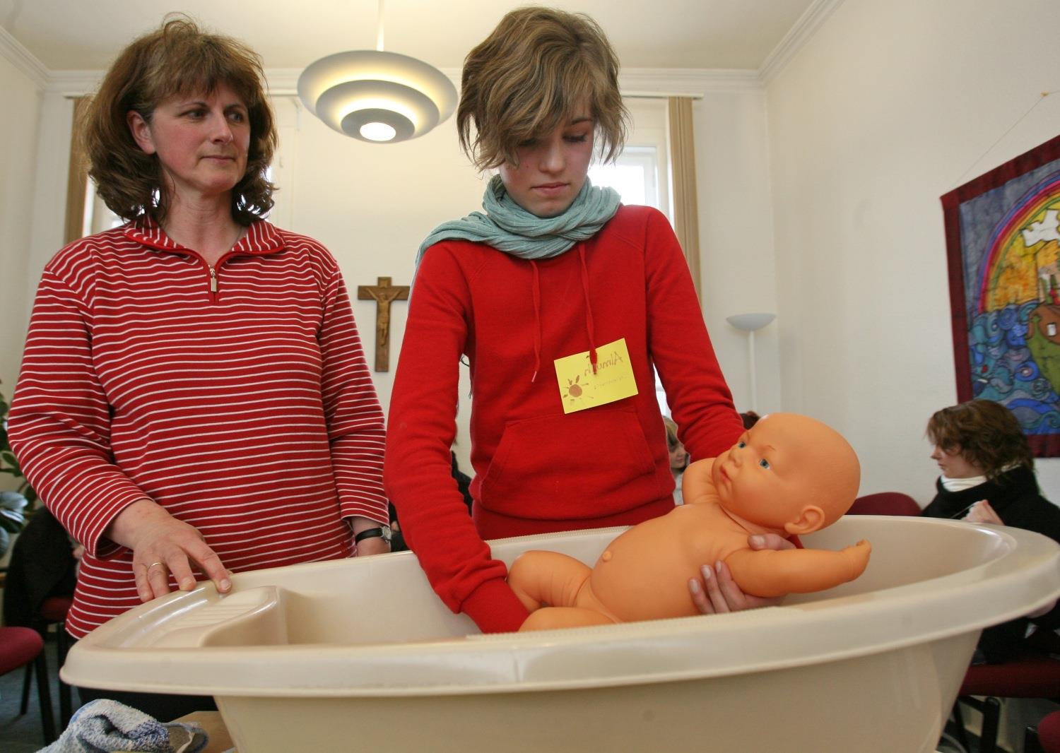 Mädchen bekommt anhand einer Puppe eine Einführung in das Waschen von Kleinkindern.