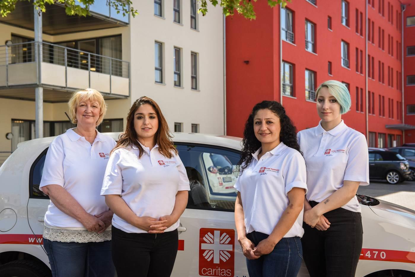Vier Mitarbeiterinnen eines ambulanten Pflegedienstes vor ihrem Dienstfahrzeug.