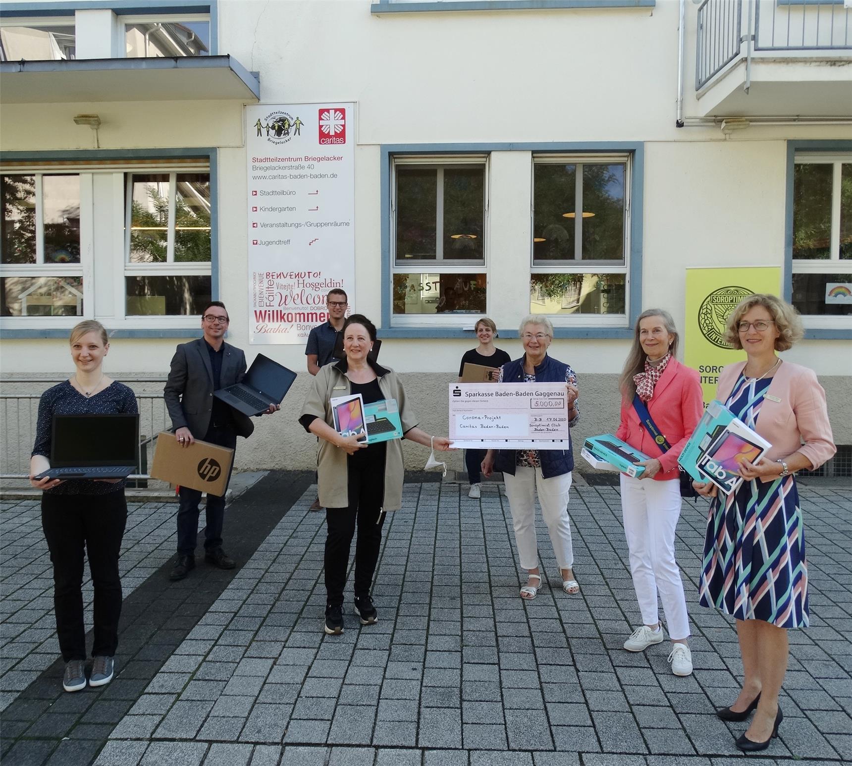 acht Frauen und Männer mit Tablets und großem Scheck