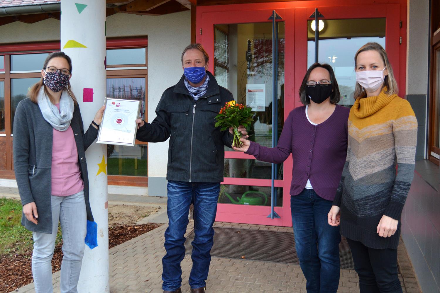 Drei Frauen und ein Mann mit Urkunde und Blumenstrauß