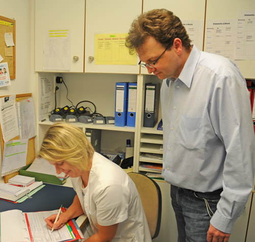 Pflegerin füllt Bogen aus, Pflegedienstleiter beobachtet sie dabei