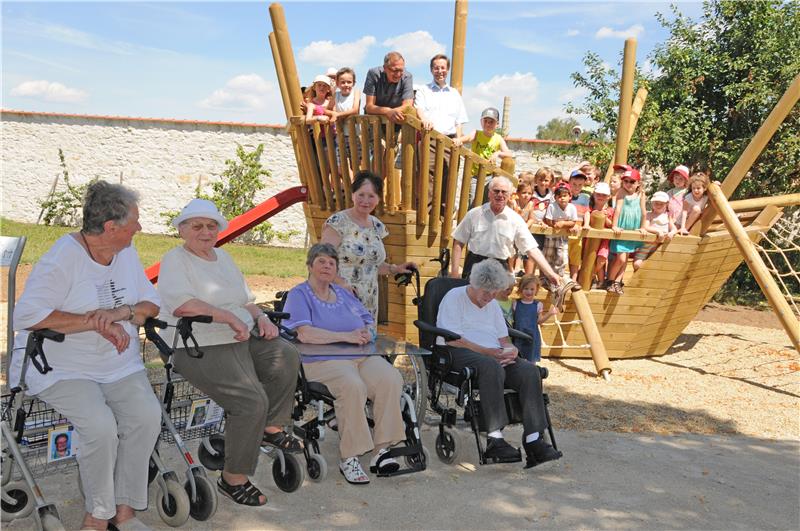 Kinder auf Spielschiff und alte Menschen in Rollstühlen davor