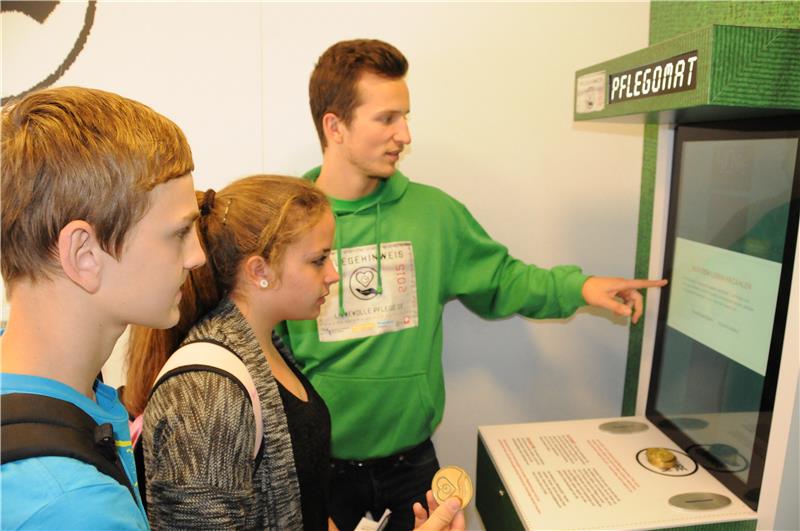 Mann erklärt Jugendlichen etwas am Pflegomaten