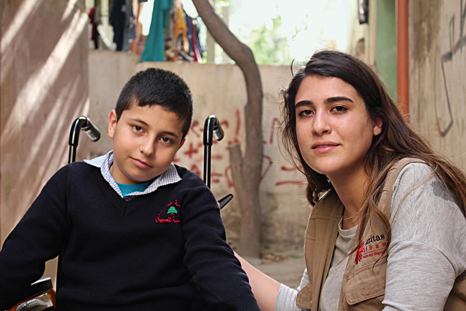 Eine Junge im Rollstuhl und eine junge Frau schauen in die Kamera.
