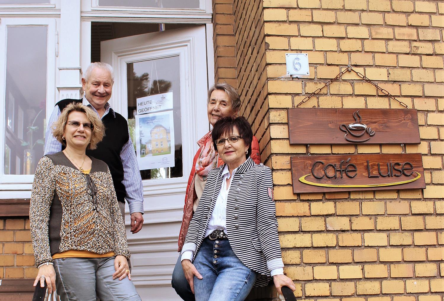 Drei Frauen und ein Mann stehen auf einer Treppe vor einer Tür.