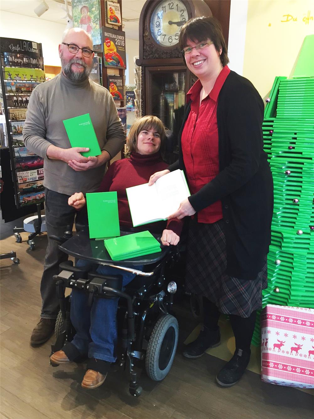 Auf dem Bild stehen zwei Erwachsene um einen Jugendlichen, der im Rollstuhl sitzt