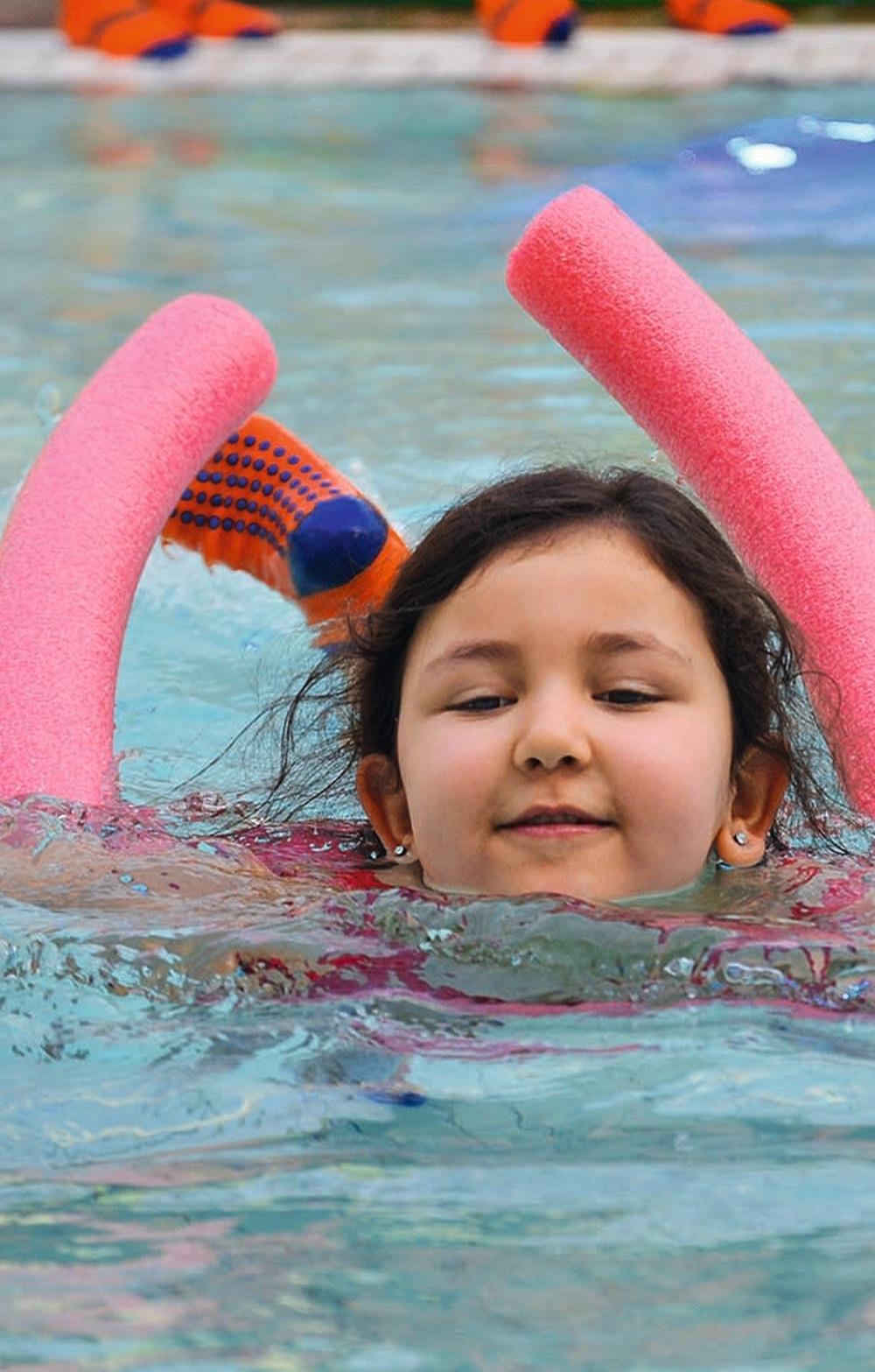 Ein Mädchen mit einer Schwimmhilfe aus Schaumstoff im Wasserbecken.