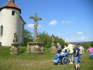Die Gruppe befindet sich auf einer Anhöhe. Vor einem Wegkreuz sucht die Gruppe Erholung in einem Spi