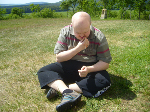 Ein Teilnehmer hat sich zurückgezogen und sitzt in Schneidersitz allein auf einer Wiese. Bei sonnige