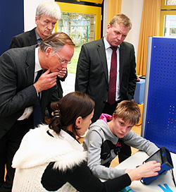 Domvikar Dr. Klaus Winterkamp neigt sich einem lernenden Schüler zu. Dahinter stehen der Schulleiter Alfred Storck und Caritas-Geschäftsführer Gregor Wortmann.