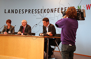 Das Bild zeigt drei Personen an einem Pult während einer Landespressekonferenz
