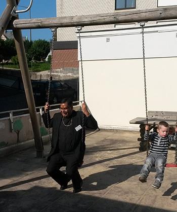Wir befinden uns auf dem Spielplatz des Kinder- und Jugendheimes. Der Bischof aus Pakistan sitzt neben einem Kind auf einer Kinderschaukel. Beide freuen sich.