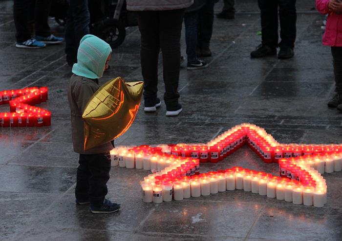 Zwei Kinder betrachten einen aus brennenden Kerzen aufgestellten Stern.