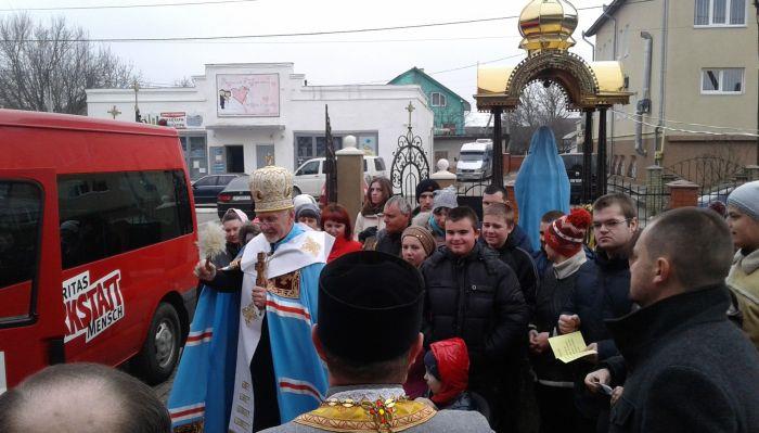 Viele behinderte Menschen stehen um den roten Ford-Transit. Der Ortsbischof in festlichem Gewand segnet diesen Bus.