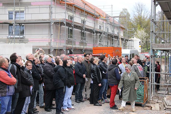 Viele Menschen stehen zwischen 2 Rohbauten und blicken auf des Dach des rechten Gebäudes. 