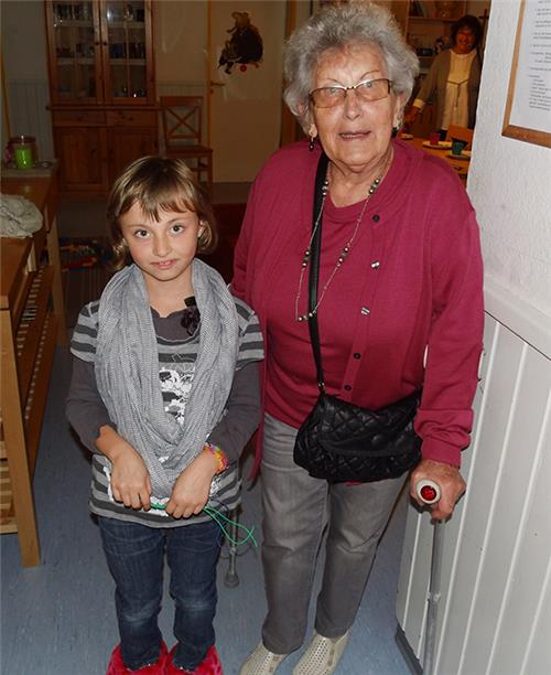 Wir befinden uns in einer der Wohngruppen im Kinderheim in Fritzlar. Eine sehr rüstige Seniorin steht gestützt auf eine Gehhilfe, neben einem Kind. Beide schauen uns bewegt an.